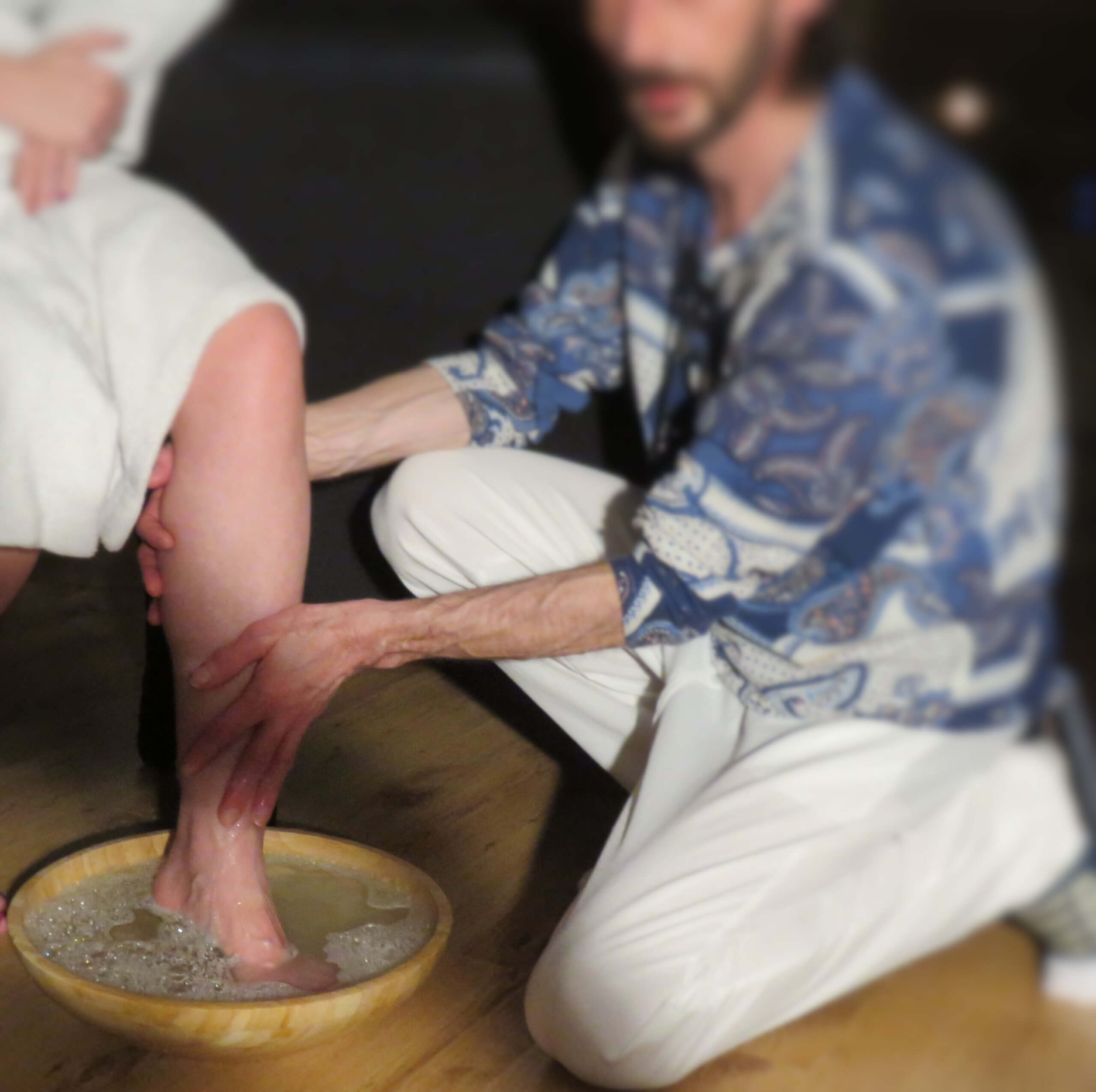 Een man met 1 voet in een voetbad. Een andere man, de eigenaar van Caress Bourdin Massage, verzorgt het voetbad.