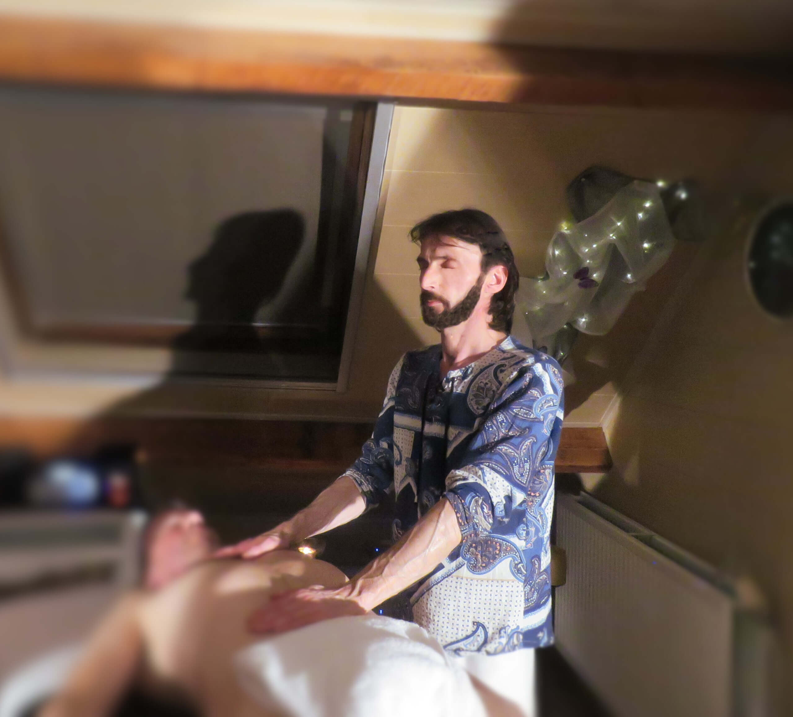 De eigenaar van Caress Bourdin Massage met beide handen op het lichaam van een man die op een massagetafel ligt. 1 hand op de buik, 1 hand op de borststreek